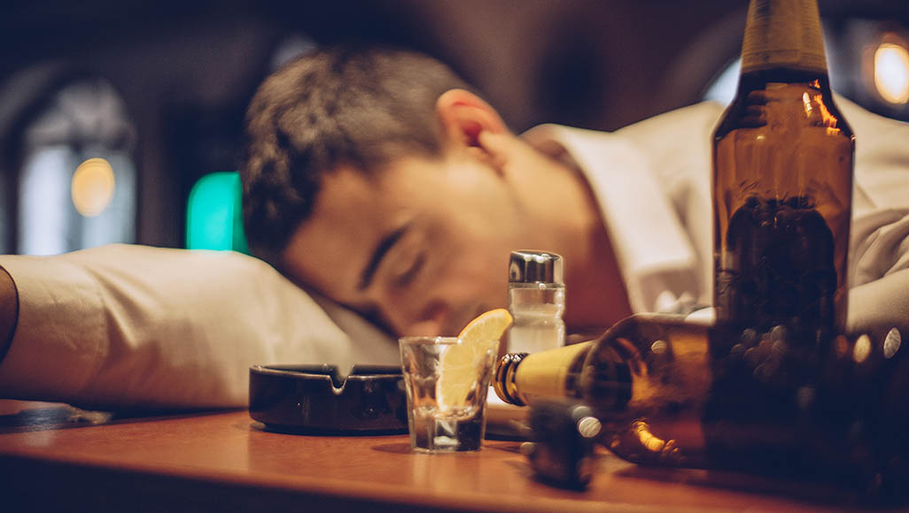 Mutélios Alcolodépendant, homme endormie à côté de bouteilles d'alcool vides.