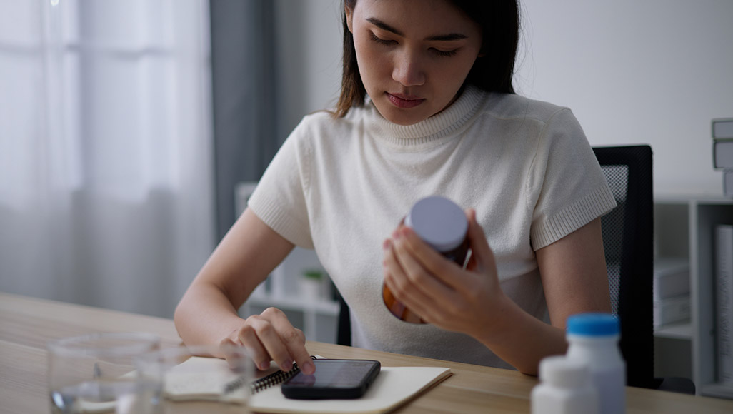 Mutélios applications pour gérer médicaments, jeune femme regardant une étiquette de médicament et notant sur son téléphone