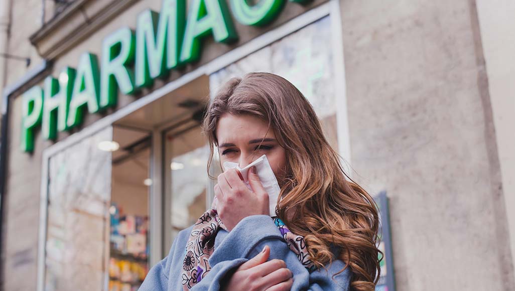 Mutélios médicaments en vente libre, femme se mouchant devant une pharmacie