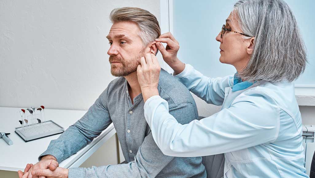 Mutélios fraude audioprothèse, femme médecin installant une prothèse auditive